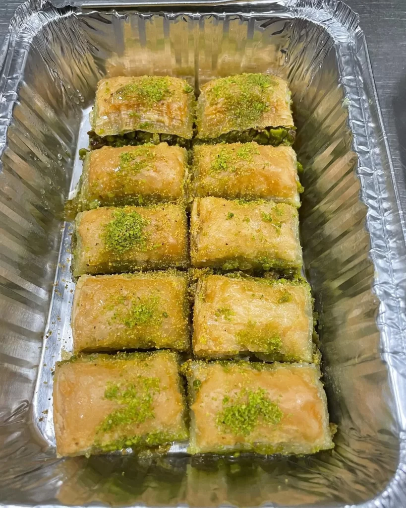Tray of pistachio baklava in syrup-soaked layers topped with ground pistachio